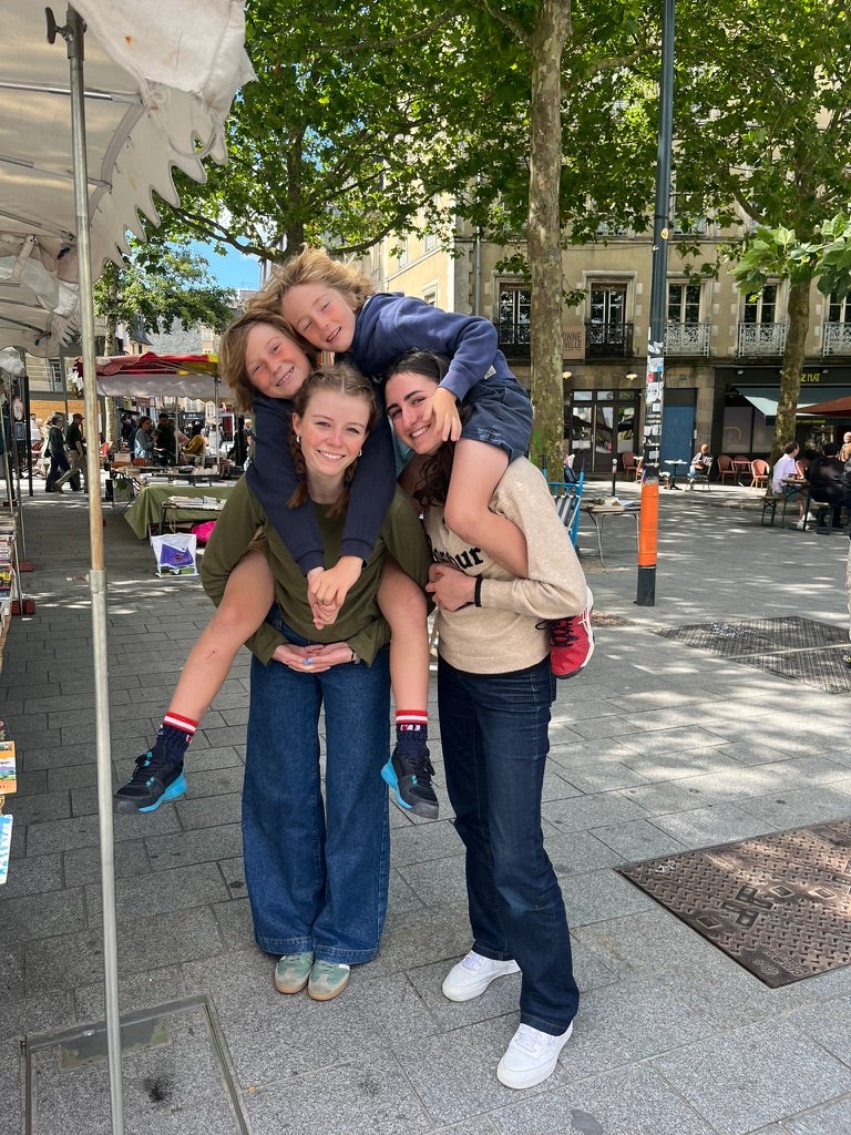 Two young women carry two boys on their shoulders at a farmers market