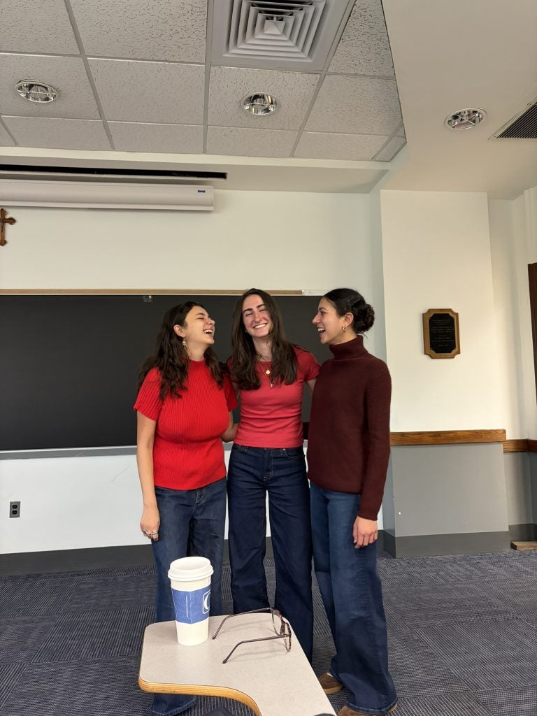 Three young women in red shirts and sweaters in a classroom