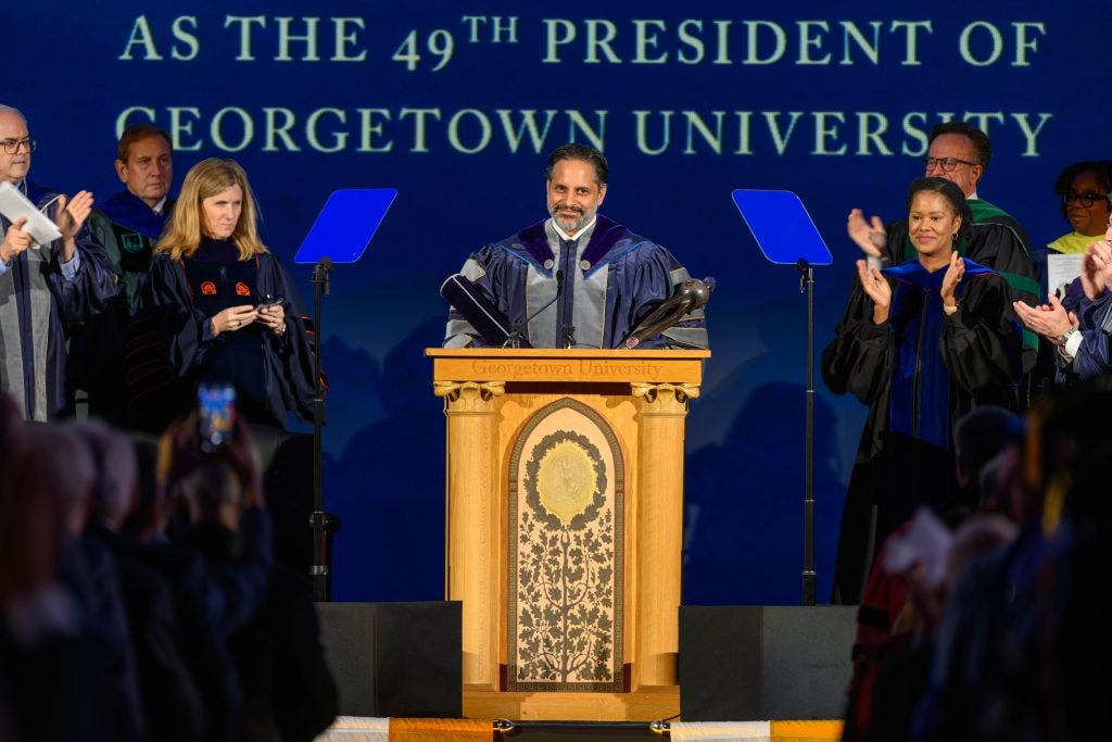 A man in purple academic robes stands behind a podium