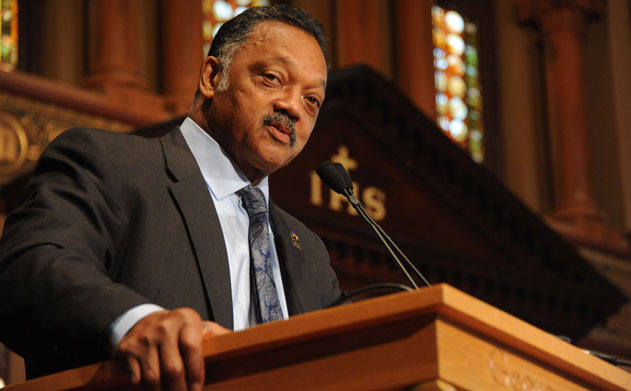 Rev. Jesse Jackson standing at podium in Gaston Hall with stained glass behind him
