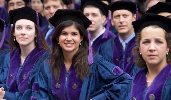A law center graduate smiles while others look on while seated