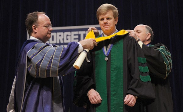 John J. DeGioia puts a hood on John Prescott while holding a scroll on stage