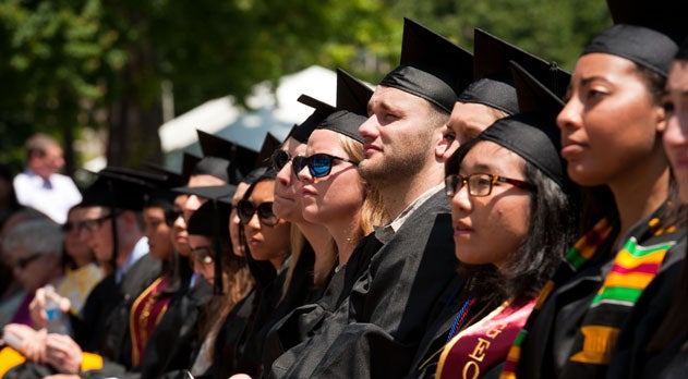 Students dressed in caps and gowns look on at commencement. 