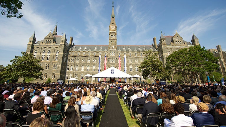 Students sitting in chairs in cap and gown on the Healy building lawn waiting for commencencement