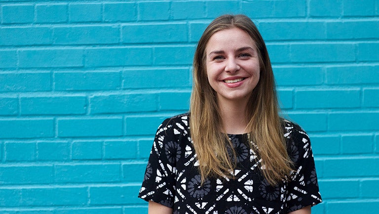 Melina Hsiao (C'18) smiles in front of a blue brick background. 