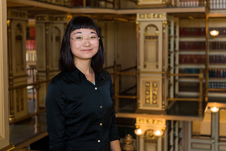 Angela Bai stands near the railing with shelves of library books in the background behind her.