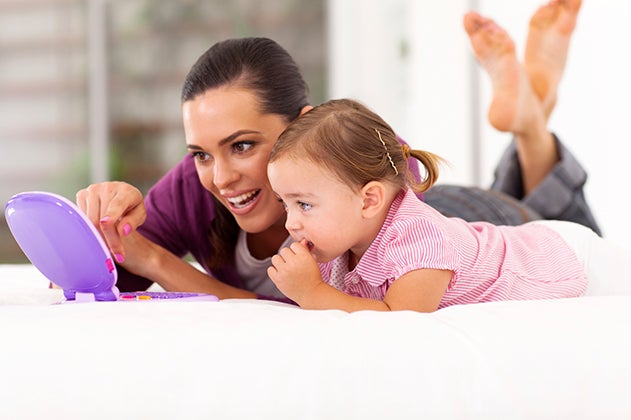 Woman and toddler lay on their stomachs watching a small screen device together