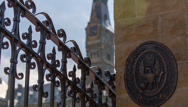 front iron gates of Georgetown with seal on concrete wall and Healy building spire in the background