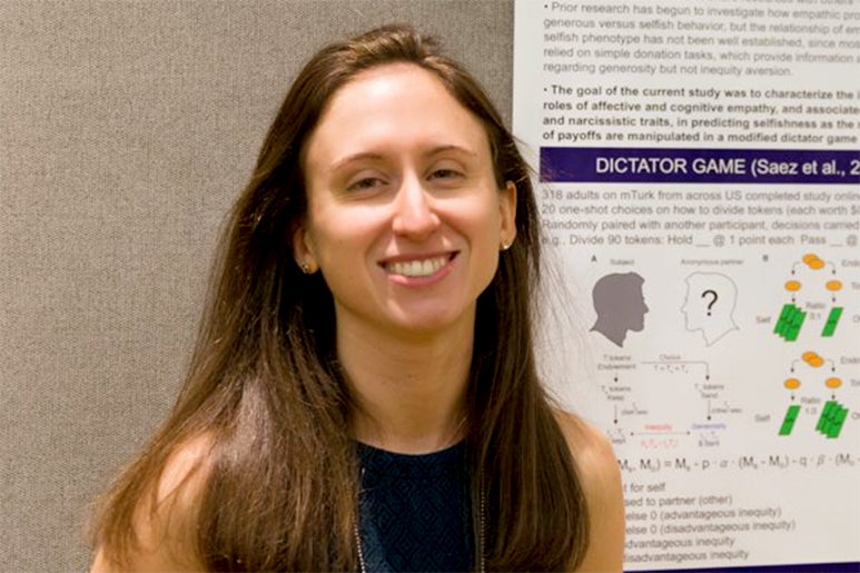 Kristin Brethel-Haurwitz smiles while standing in front of a psychology poster.