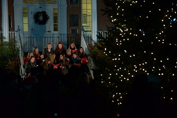 Singers stand on the steps of Old North with a door to the building in the background while others listen below