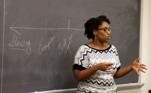 Marcia Chatelain in front a classroom chalkboard with the words "slavery, emancipation, and Great Migration" written on it.