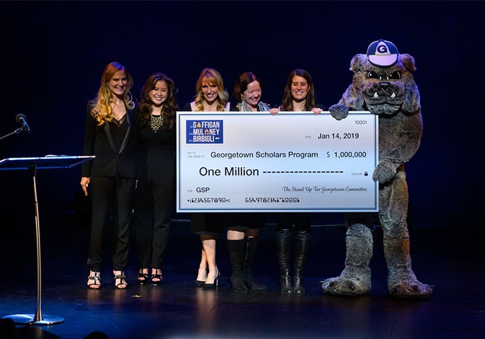 A group of Georgetown alumni stand with the school mascot on stage holding up a check for $1 million.