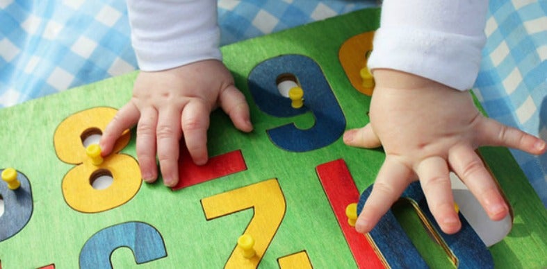 A photo of a baby's hands on top of a colorful puzzle.