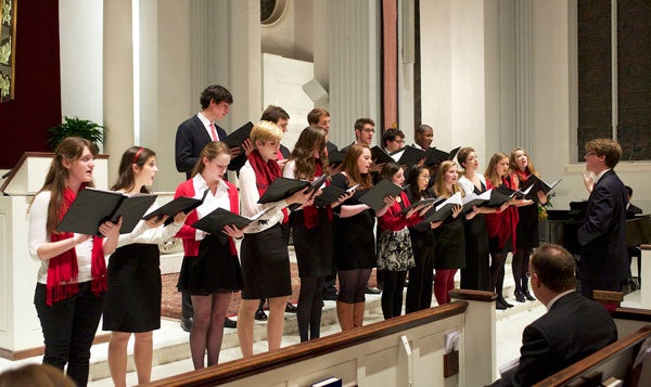 A conductor leads a choir holding their music folders in a church