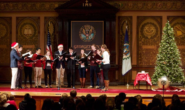 Singers stand in a semicircle on stage in Gaston Hall wearing Christmas regalia