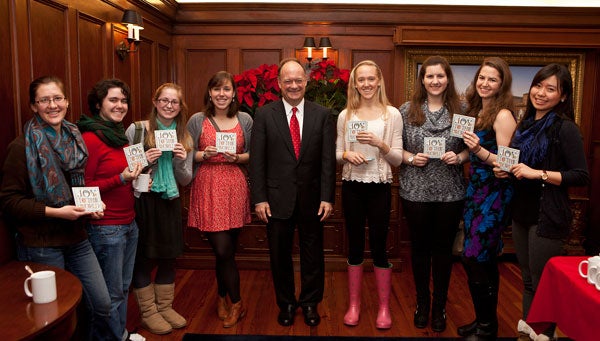 John J. DeGioia stands with students holding a copy of the new holiday album in a room