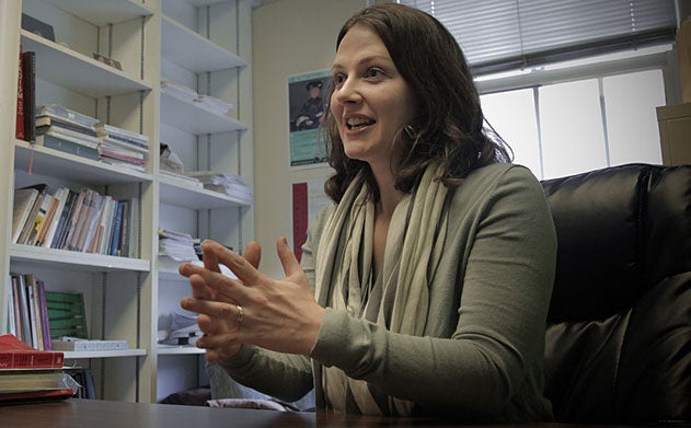 Erin Cline sits at a desk speaking and gesturing with her hands with a bookshelf in the background