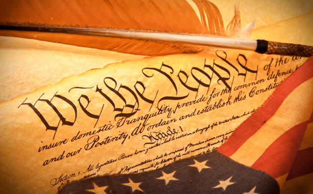 A quill pen sits on a copy of the United States Constitution