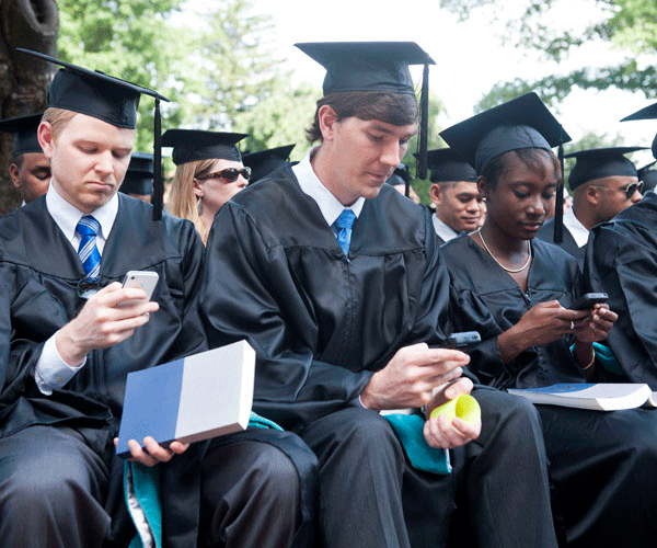 SCS Graduates with cell phones while seated on Healy Lawn
