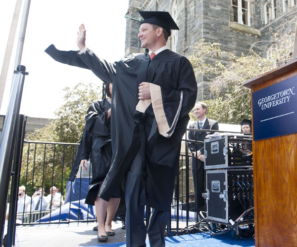 MBA Graduate waves to crowd while walking across stage on Healy Lawn