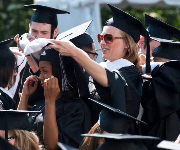 Graduates help each other don hoods during ceremony on Healy Lawn