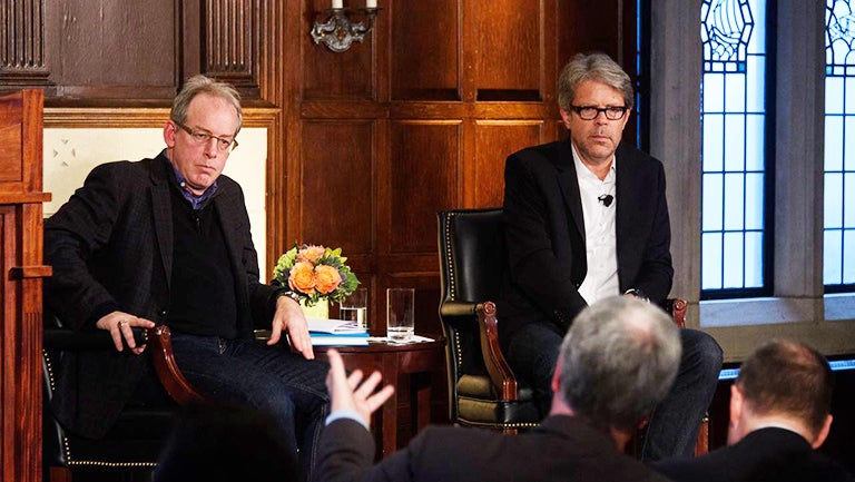 Paul Elie and Jonathan Franzen sit on stage listening to a member of the audience who is gesturing with one hand