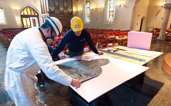 Workers cut out loosely woven scrims to temporarily replace the removed stained glass images while they are being repaired.