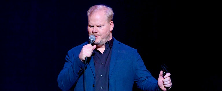 Jim Gaffigan speaks into the microphone while on stage.