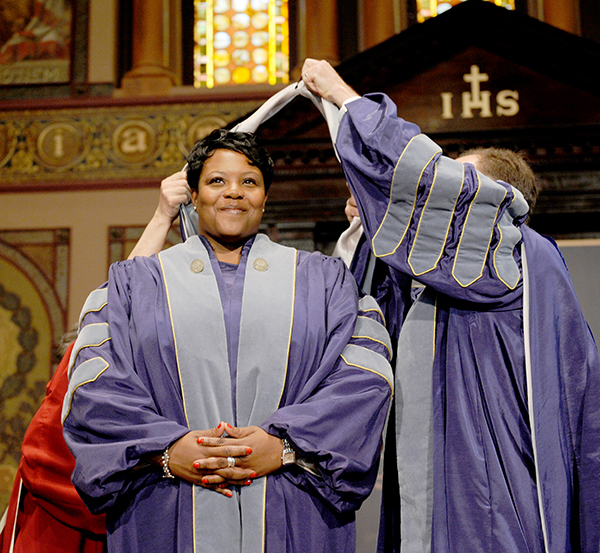 Kaya Henderson is hooded in her academic regalia on stage by Georgetown President John J. DeGioia leadership.