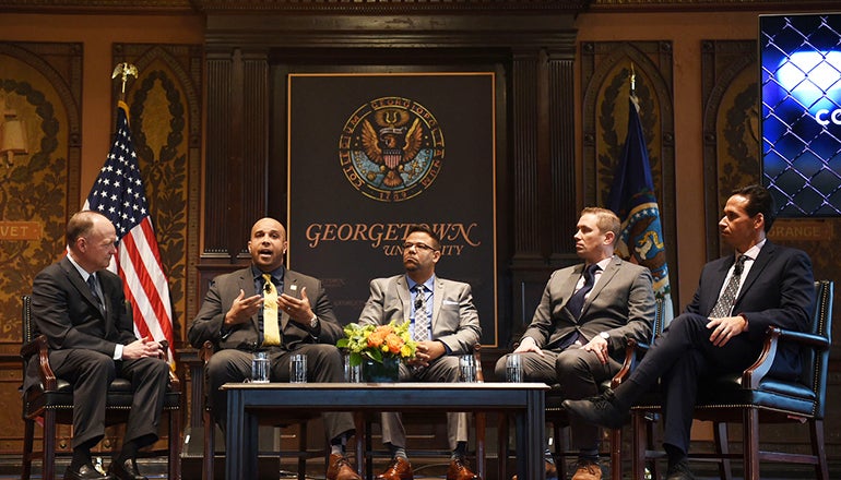 John J. DeGioia, Brian Ferguson, George Chochos, Shon Hopwood and Marc Howard on stage with flag and Georgetown University sign