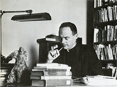 Rev. William McFadden, S.J. sitting at a desk holding pen in 1967