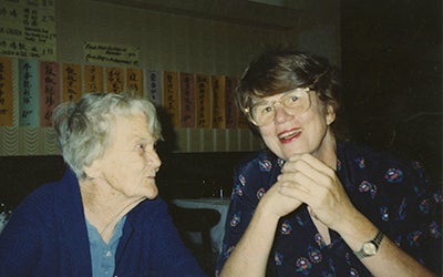 Janet Reno sitting with an elderly woman and smiling into the camera