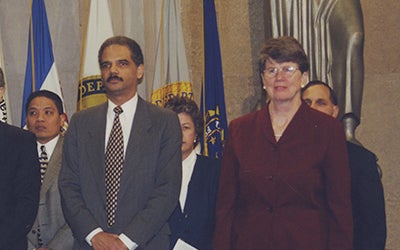 Janet Reno with Eric Holder, standing with others in front of flags