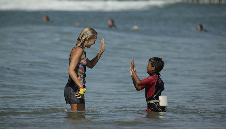 Emi Koch in the ocean high-fiving a young boy