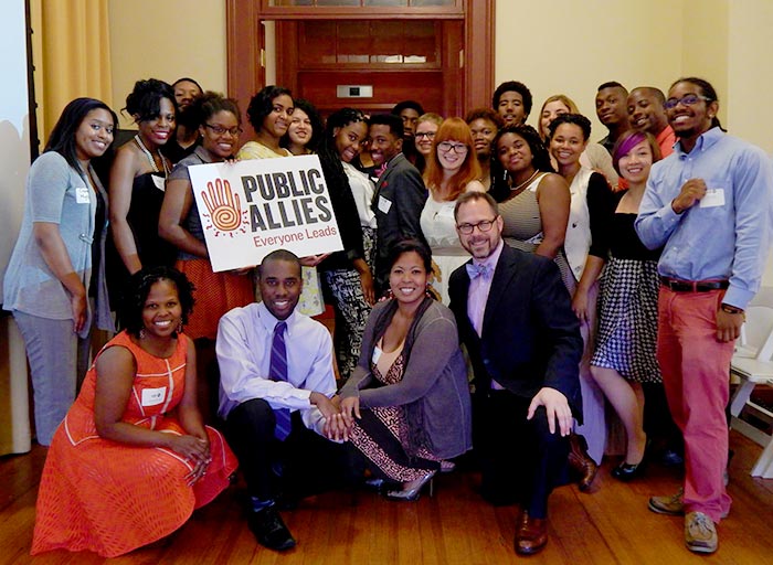 Nakeisha Neal Jones poses with some of her graduating Public Allies students as they hold up a sign that says Everyone Leads