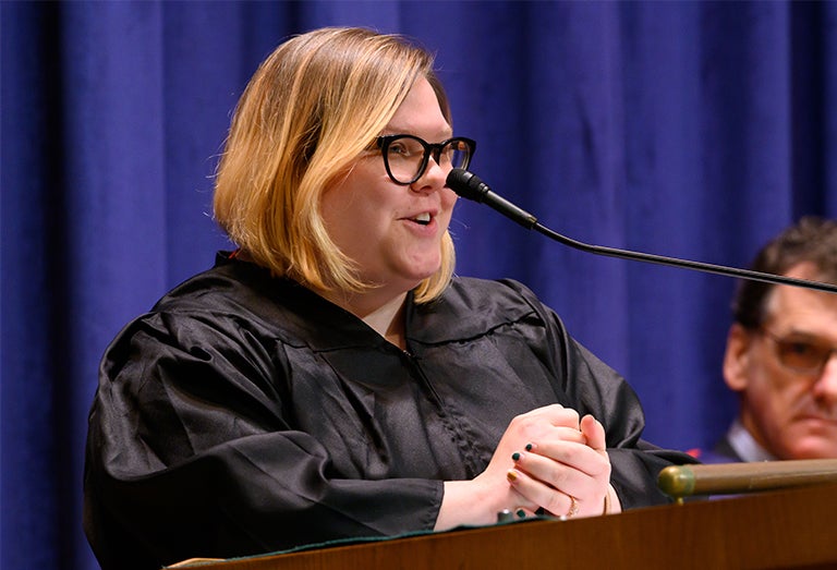 Amanda Scott speaks to the audience through a microphone in front of a blue backdrop.