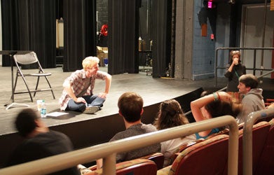 Michael Benz sits on a stage and talks to students who are seated in theater