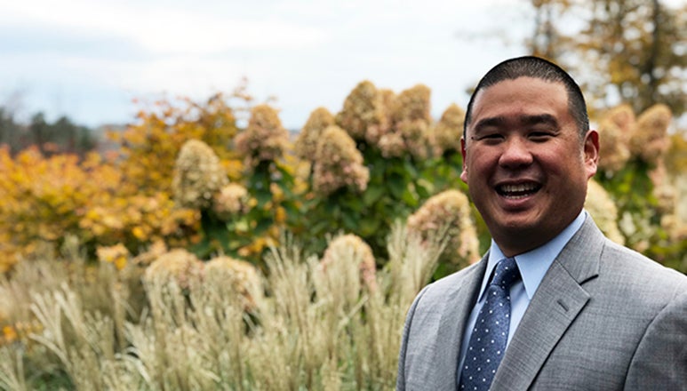 Ben Kuo standing in front of a field with blue sky and trees in the background