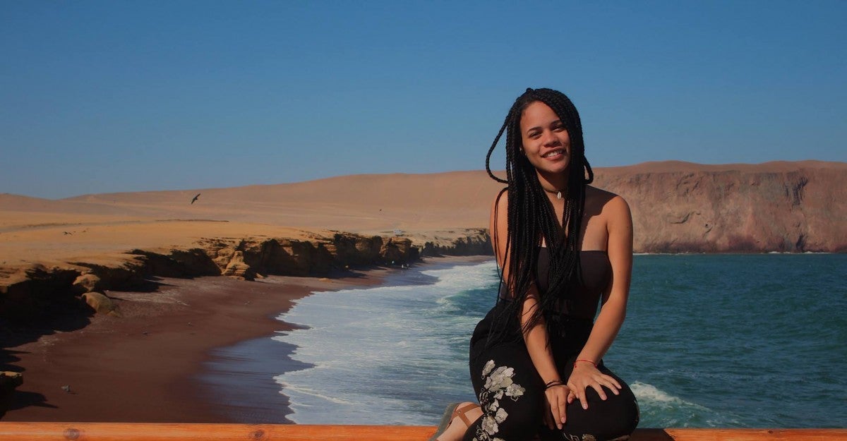 Bianca Uribe sits surrounded by a beach with an expansive blue sky in the background.