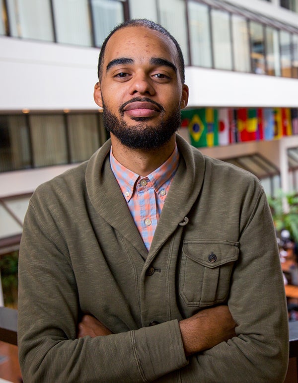 Marcus Board looks into the camera with a smile as office windows and international flags appear in the background