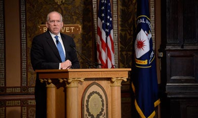 John Brennan speaks behind a podium on Gaston Hall's stage.