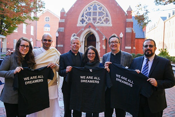 Rev. Olivia Lane, Brahmachari VraJvihari Sharan, Rev. Gregory Schenden, S.J., Rabbi Rachel Gartner, Rev. Bryant M. Oskvig and Imam Yahya Hendi stand in front of Dahlgren Chapel holding black t-shirts that say "We Are All Dreamers" on them.