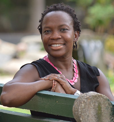 Charlene Brown-McKenzie sits on a bench with her arm propped up in the back smiling toward the camera.