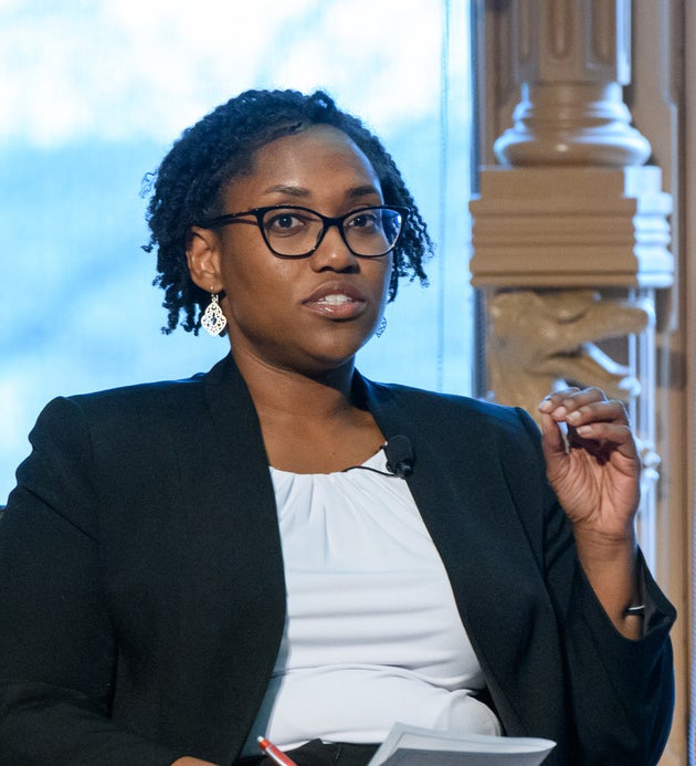 Marcia Chatelain wears glasses while talking on stage with a windows showing outdoor foliage in the background.