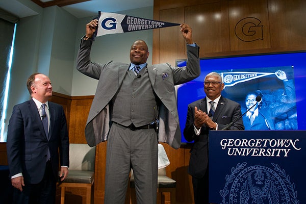 Patrick Ewing (C'85) holds up Georgetown University banner as President DeGioia and Lee Reed, Georgetown’s director of intercollegiate athletics, look on