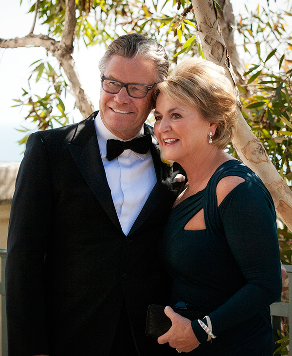 Peter and Susan Cooper stand under a tree and pose in formal clothes for a photo.
