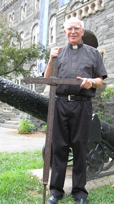 Rev. Murphy stands with the Iron Cross in front of Healy Hall.