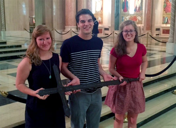 Three smiling Georgetown undergraduates hold the Iron Cross.