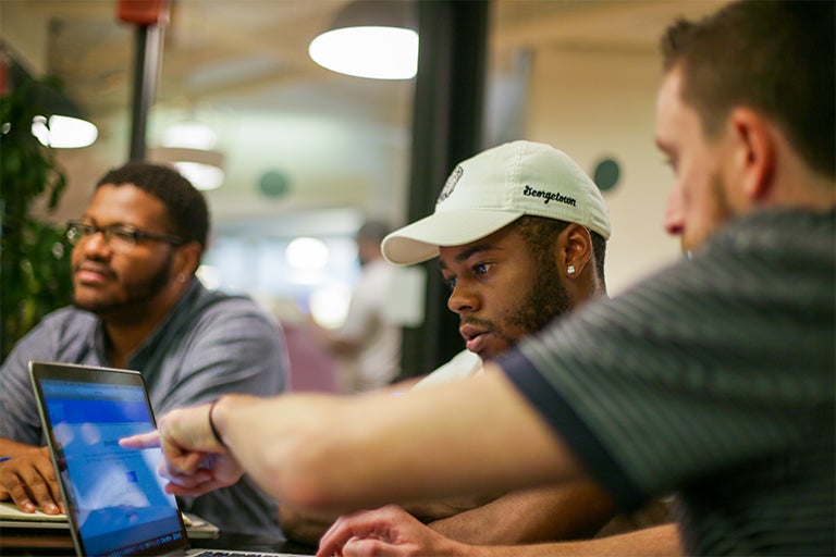 Jerome Small sits looking off to the left as Derron Payne sits looking at his laptop with a entrepreneurial mentor.