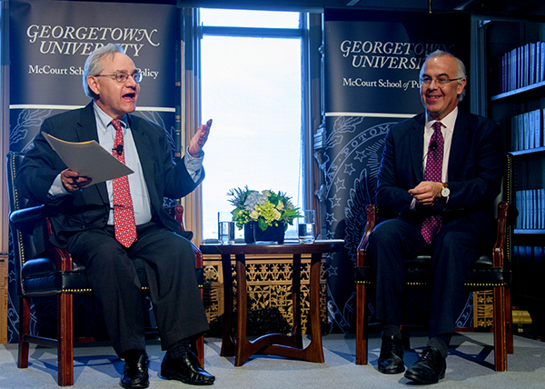 E.J. Dionne speaks on stage while seated with David Brooks, also seated, on the right.